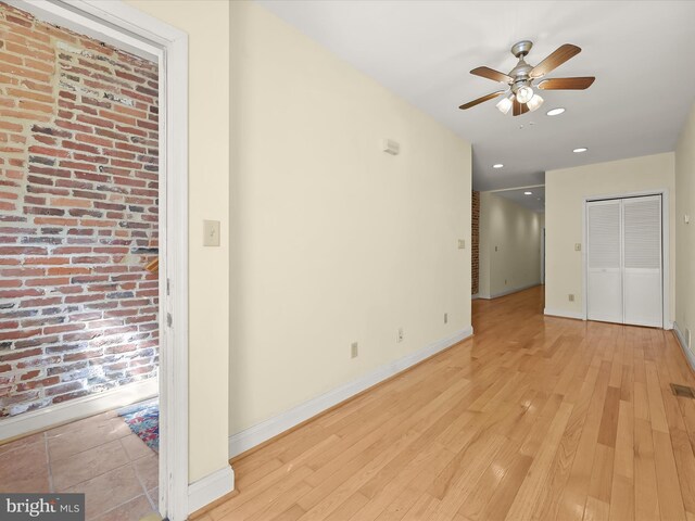 interior space featuring light wood-type flooring, brick wall, baseboards, visible vents, and ceiling fan
