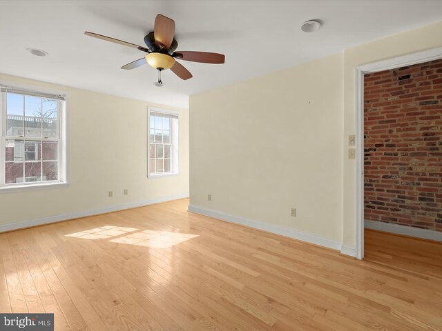spare room featuring brick wall, baseboards, and light wood-style floors