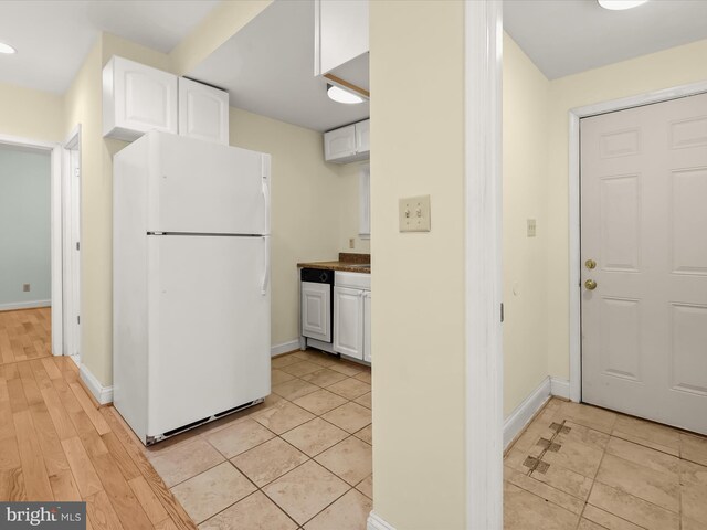 kitchen with freestanding refrigerator, white cabinets, light tile patterned floors, and baseboards