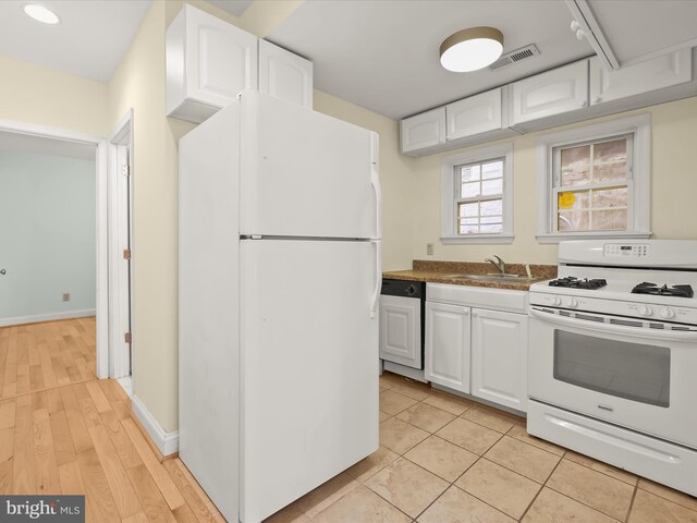kitchen with white cabinets, white appliances, baseboards, dark countertops, and a sink