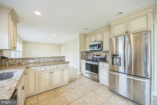 kitchen featuring light stone counters, tasteful backsplash, a peninsula, stainless steel appliances, and cream cabinetry