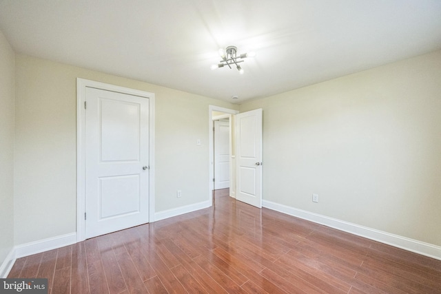 unfurnished bedroom with baseboards, a notable chandelier, and wood finished floors
