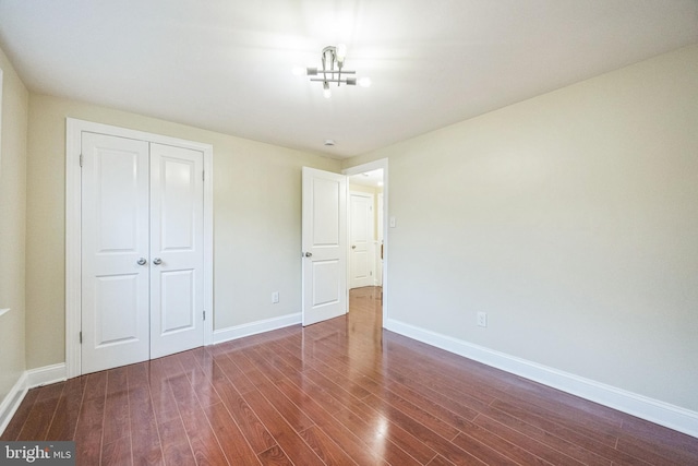 unfurnished bedroom with dark wood-style flooring, baseboards, and a closet