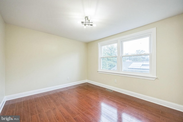 spare room with dark wood-style floors, visible vents, and baseboards