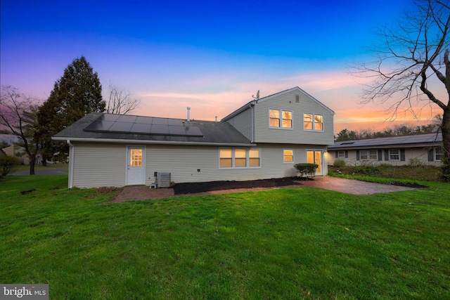 back of property at dusk featuring cooling unit, a patio, solar panels, and a lawn