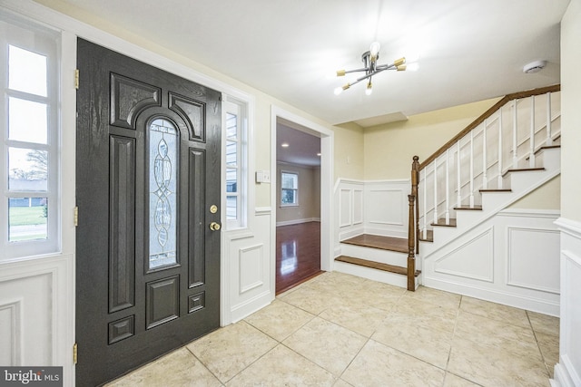 foyer entrance with a decorative wall, stairway, a notable chandelier, and a wealth of natural light