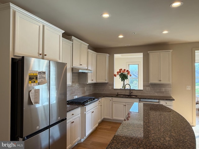 kitchen with black gas stovetop, freestanding refrigerator, under cabinet range hood, light wood finished floors, and a sink