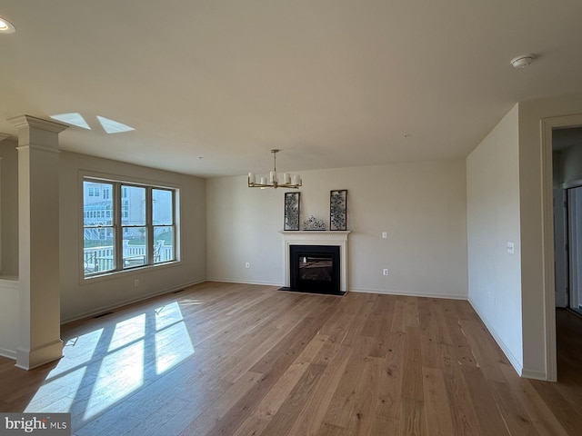 unfurnished living room featuring a notable chandelier, baseboards, a fireplace with flush hearth, visible vents, and wood finished floors