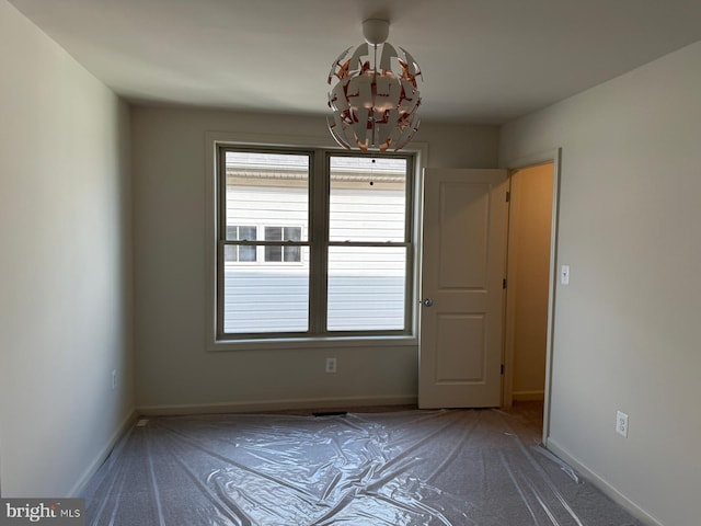 carpeted spare room featuring a notable chandelier and baseboards