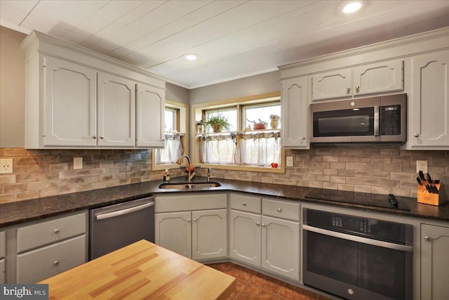 kitchen featuring dark tile patterned flooring, stainless steel appliances, a sink, and tasteful backsplash