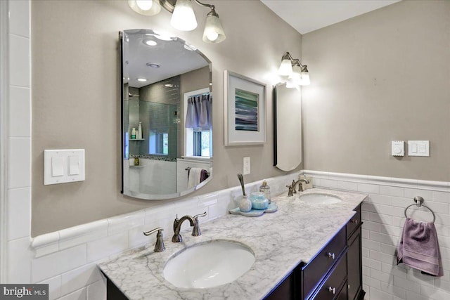 full bath featuring double vanity, tile walls, a sink, and a shower with shower door