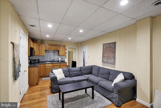 living area featuring light wood-type flooring, a paneled ceiling, and visible vents