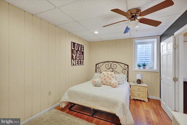bedroom with baseboards, ceiling fan, wood finished floors, and a paneled ceiling
