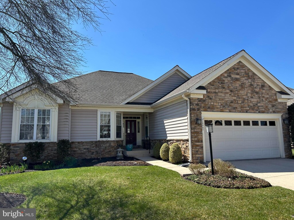 view of front of house with roof with shingles, a front yard, stone siding, an attached garage, and driveway