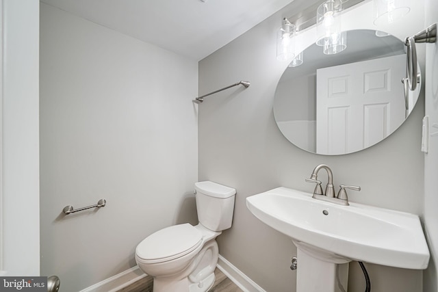 bathroom featuring toilet, a sink, baseboards, and wood finished floors
