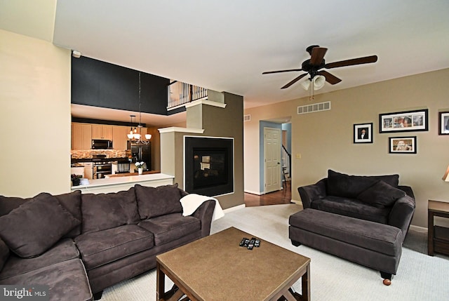 living area featuring visible vents, baseboards, a multi sided fireplace, and ceiling fan with notable chandelier