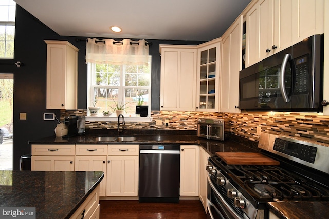 kitchen with stainless steel appliances, tasteful backsplash, a sink, and dark stone counters