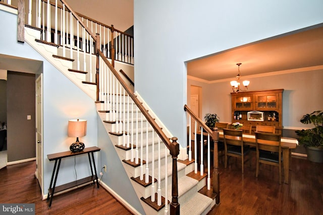 staircase featuring baseboards, a notable chandelier, crown molding, a towering ceiling, and wood finished floors