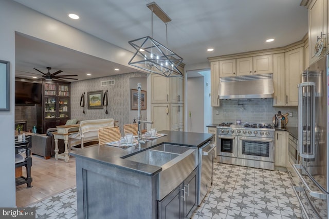 kitchen with under cabinet range hood, premium appliances, cream cabinetry, light flooring, and wallpapered walls