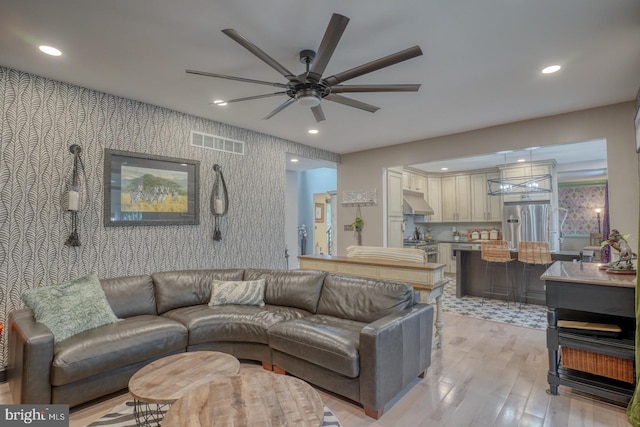 living room featuring wallpapered walls, ceiling fan, light wood finished floors, an accent wall, and recessed lighting
