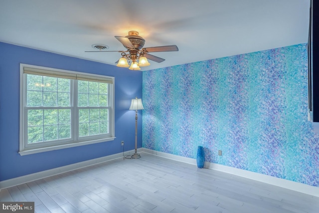 spare room featuring wallpapered walls, baseboards, wood finished floors, and ceiling fan