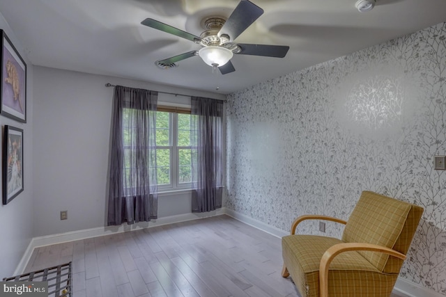 living area featuring wallpapered walls, wood finished floors, a ceiling fan, and baseboards