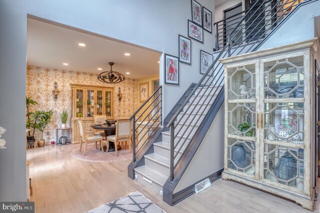 stairs featuring wallpapered walls, wood finished floors, recessed lighting, baseboards, and a chandelier