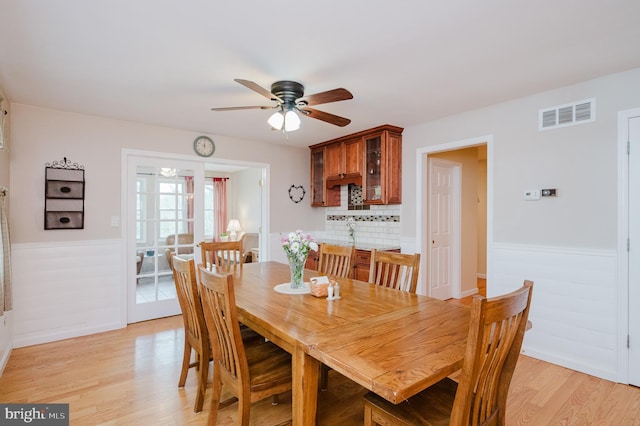 dining space with light wood-style floors, visible vents, a wainscoted wall, and ceiling fan