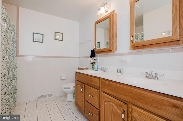 bathroom featuring tile patterned flooring, visible vents, toilet, a sink, and tile walls