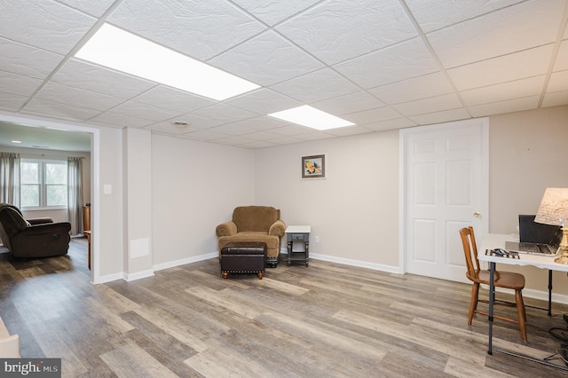 living area with baseboards, wood finished floors, and a drop ceiling