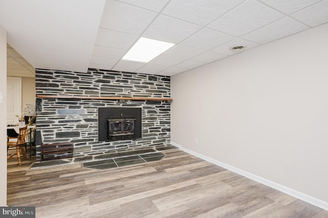 interior space featuring a paneled ceiling, baseboards, visible vents, wood finished floors, and a wood stove