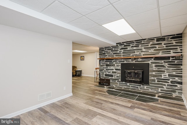 unfurnished living room with a drop ceiling, wood finished floors, a wood stove, visible vents, and baseboards