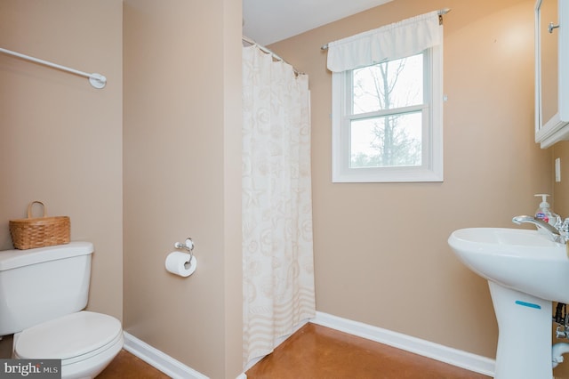 bathroom featuring baseboards, curtained shower, a sink, and toilet