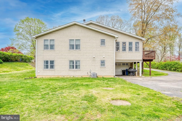 rear view of property with cooling unit, a garage, a deck, a yard, and aphalt driveway