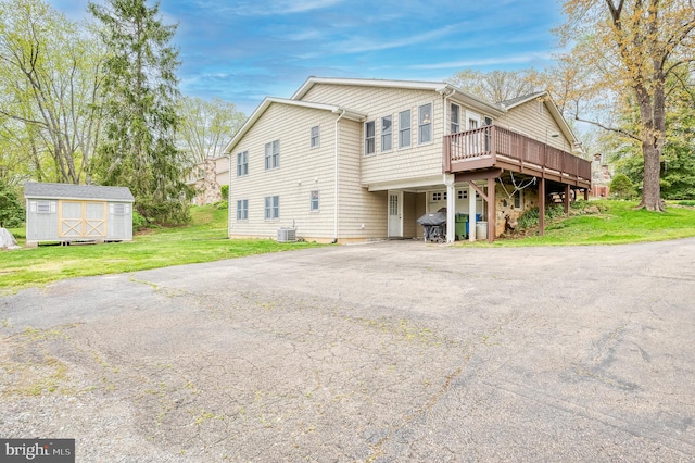 exterior space featuring driveway, a deck, an outbuilding, a yard, and a storage unit