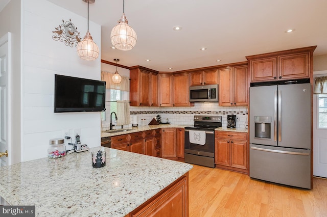 kitchen featuring light stone counters, brown cabinetry, stainless steel appliances, and a sink