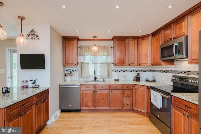 kitchen featuring tasteful backsplash, a sink, brown cabinetry, decorative light fixtures, and appliances with stainless steel finishes