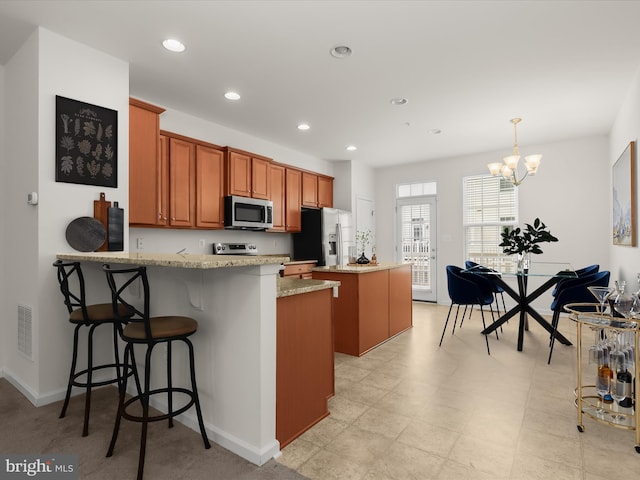 kitchen with brown cabinetry, fridge with ice dispenser, stainless steel microwave, visible vents, and a kitchen island
