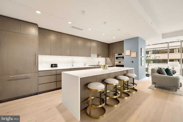 kitchen featuring a sink, light wood-style floors, a breakfast bar, decorative backsplash, and recessed lighting