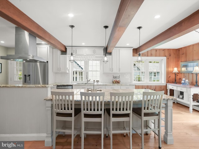 kitchen with light wood finished floors, light stone counters, island range hood, beam ceiling, and appliances with stainless steel finishes