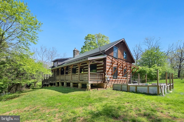 rear view of property featuring a lawn, a chimney, and roof with shingles
