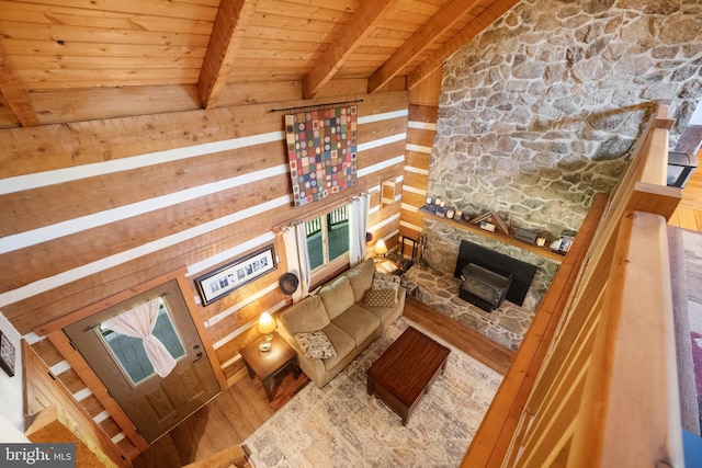 living area with wood finished floors, a stone fireplace, wooden walls, vaulted ceiling with beams, and wood ceiling