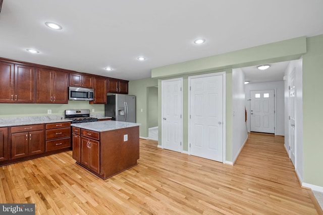 kitchen with a kitchen island, baseboards, appliances with stainless steel finishes, and light wood-style floors