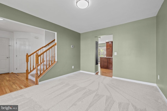 unfurnished room with stairs, baseboards, light colored carpet, and light wood finished floors