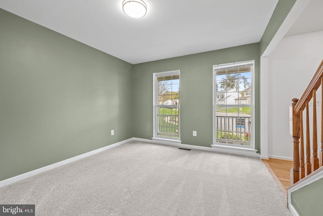 carpeted empty room featuring baseboards, stairs, and visible vents
