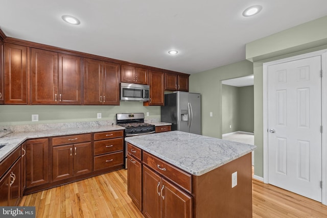 kitchen featuring a kitchen island, stainless steel appliances, light stone countertops, and light wood-type flooring