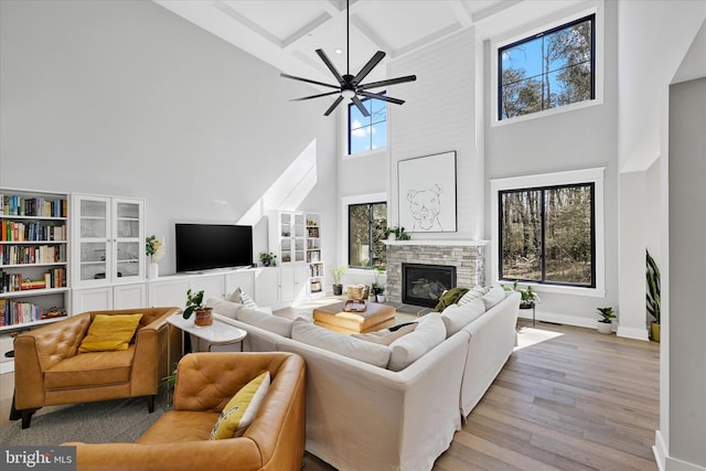 living room featuring a stone fireplace, baseboards, coffered ceiling, and light wood finished floors