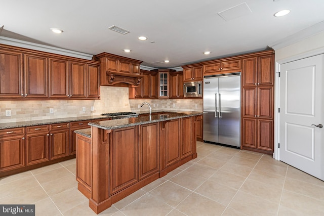 kitchen featuring light tile patterned flooring, a breakfast bar, brown cabinets, dark stone counters, and built in appliances
