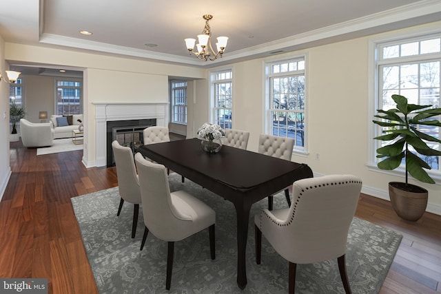 dining area with dark wood-style flooring, ornamental molding, a glass covered fireplace, and a notable chandelier