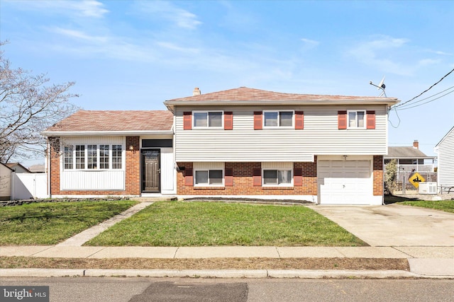 split level home with fence, a garage, concrete driveway, a front yard, and brick siding